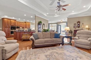 living area featuring a tray ceiling, crown molding, recessed lighting, ceiling fan, and light wood-type flooring