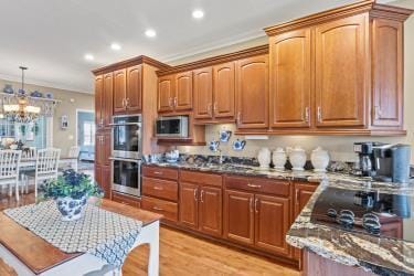 kitchen with stone countertops, light wood-style flooring, stainless steel appliances, decorative light fixtures, and crown molding