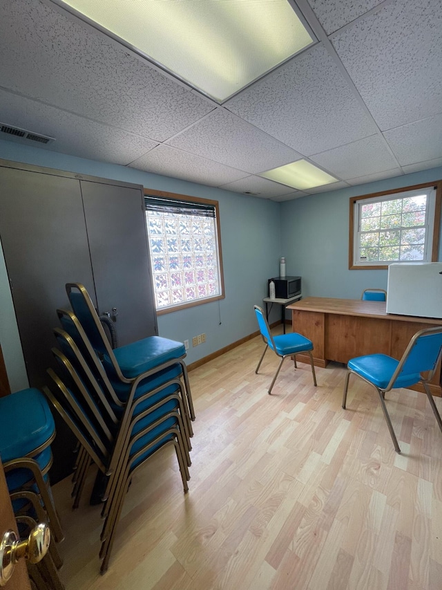 office area with light wood-type flooring, a paneled ceiling, and a wealth of natural light