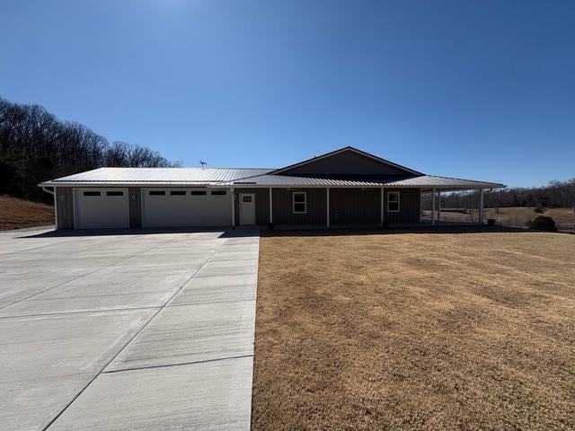 view of front of house with a front lawn, concrete driveway, metal roof, and an attached garage