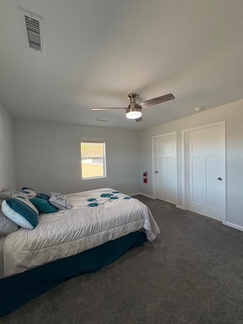 bedroom featuring visible vents, dark carpet, baseboards, and ceiling fan