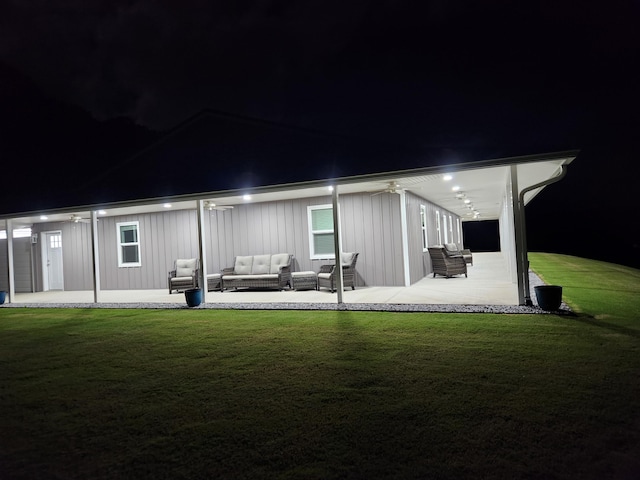 back of house at night with board and batten siding, a yard, a patio, and an outdoor hangout area