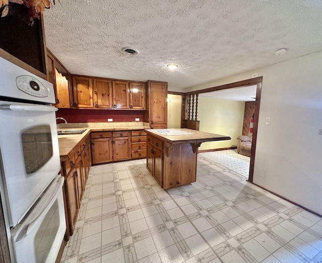 4140 Chavis Rd, Cosby, TN 37722 - kitchen featuring oven, brown cabinetry, a kitchen island, light floors, and a textured ceiling