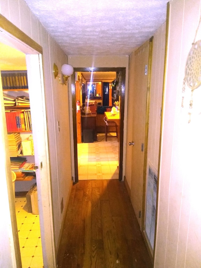 hall with hardwood / wood-style flooring, wood walls, and a textured ceiling