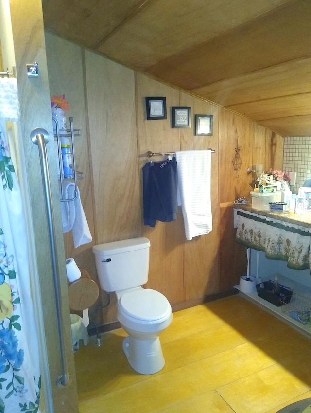 bathroom with wood walls, vaulted ceiling, and toilet