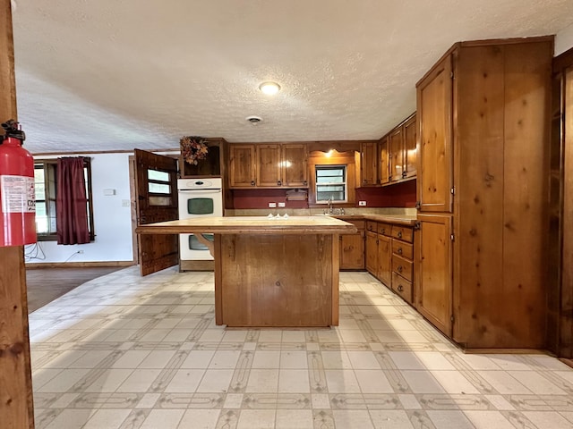 4140 Chavis Rd, Cosby, TN 37722 - kitchen featuring white double oven, light floors, a kitchen island, a textured ceiling, and brown cabinetry