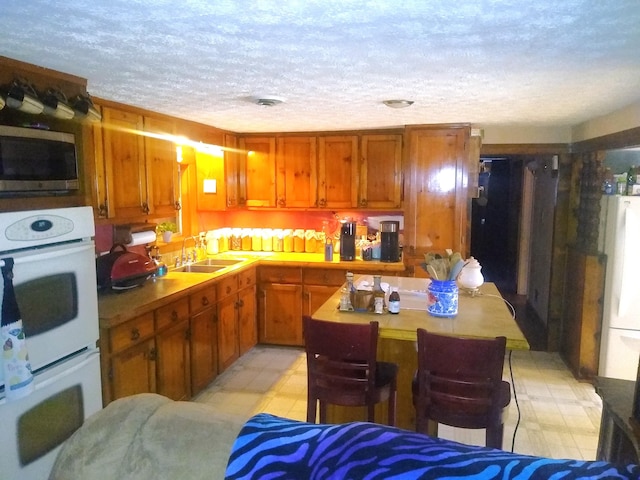 kitchen with a textured ceiling, white appliances, a center island, and sink