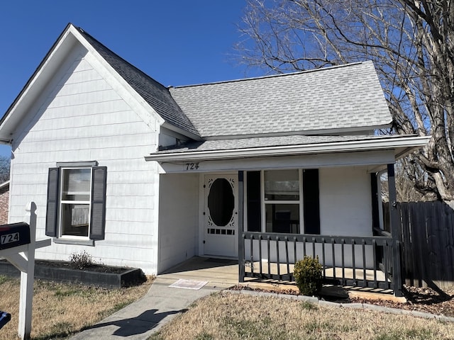 view of front of house featuring a porch, a shingled roof, and fence