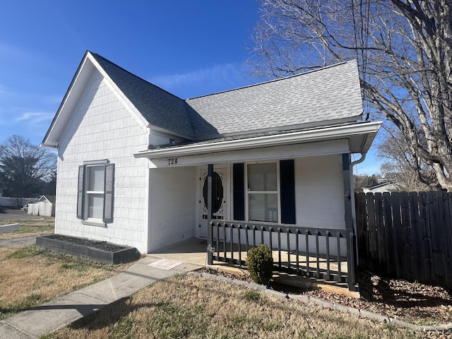 view of front of home with a porch, roof with shingles, and fence