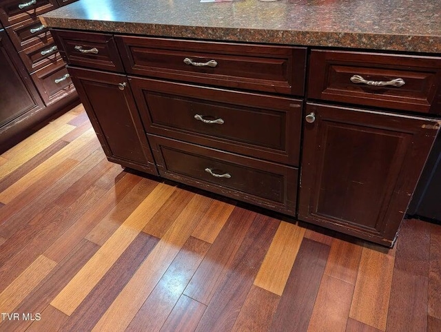 room details with dark brown cabinetry, dark stone counters, and light wood-type flooring