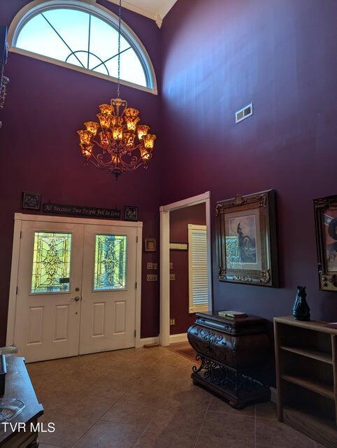 tiled entrance foyer with french doors, a chandelier, and a high ceiling