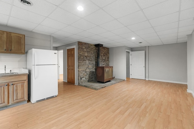 2935 Glendale Community Rd, Greenback, TN 37742 - unfurnished living room featuring a wood stove, light wood-type flooring, a sink, baseboards, and a paneled ceiling