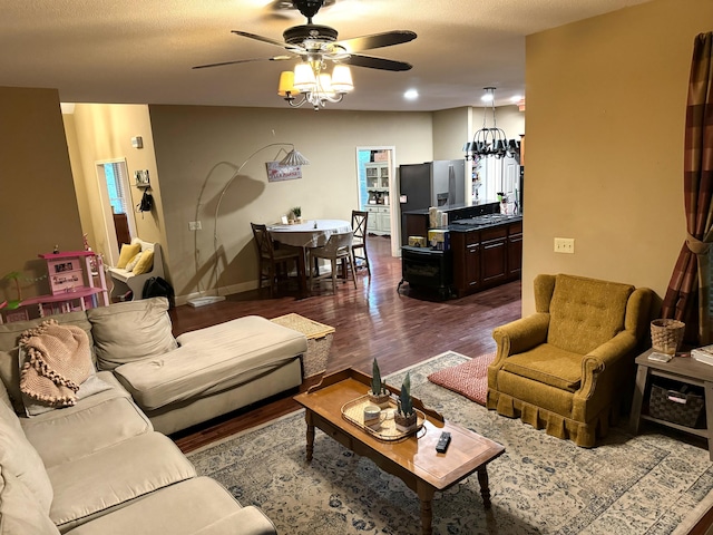 living room featuring a ceiling fan, a textured ceiling, baseboards, and dark wood-style flooring