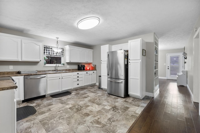 kitchen featuring a textured ceiling, stainless steel appliances, sink, white cabinets, and hanging light fixtures