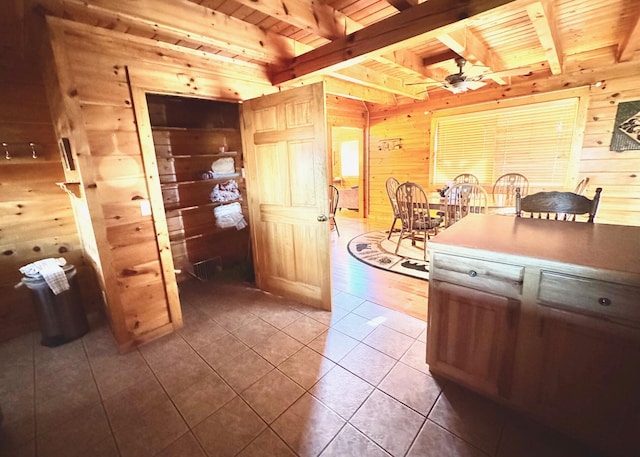 kitchen featuring a ceiling fan, wood ceiling, wooden walls, tile patterned flooring, and beamed ceiling