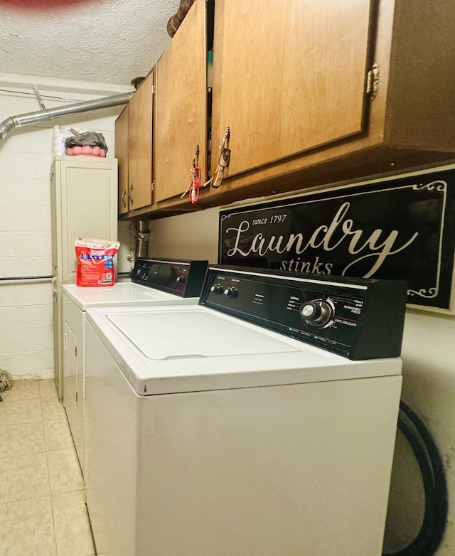 washroom featuring washer and clothes dryer, a textured ceiling, cabinet space, light tile patterned floors, and concrete block wall