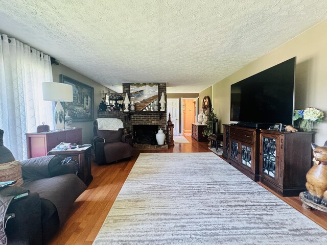 living room featuring a textured ceiling, a brick fireplace, and wood finished floors