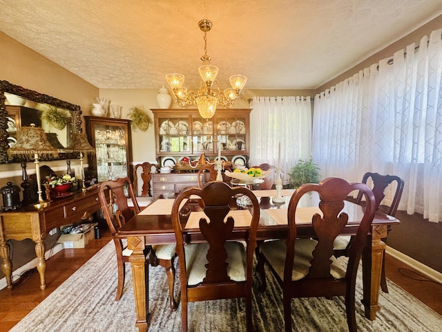 dining area with baseboards, a textured ceiling, wood finished floors, and a notable chandelier