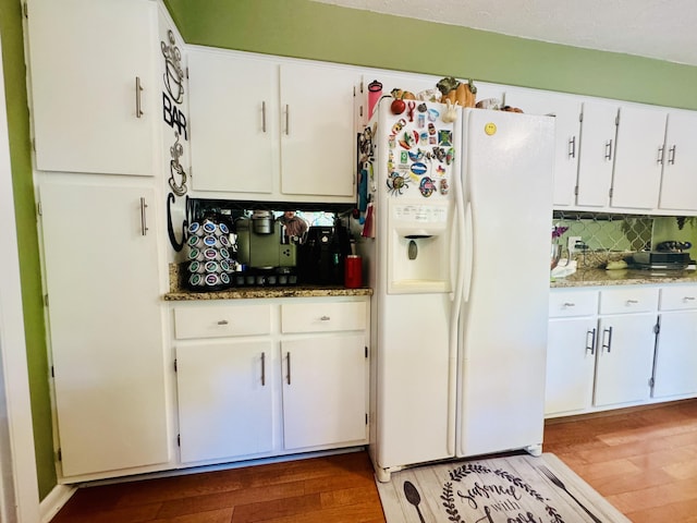 kitchen featuring backsplash, wood finished floors, stone countertops, white cabinets, and white fridge with ice dispenser