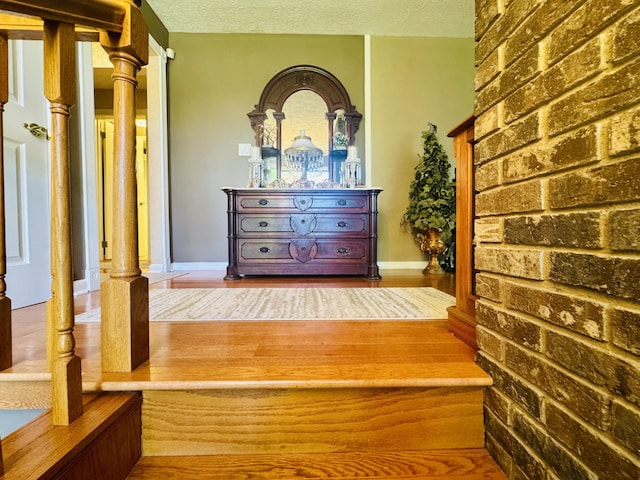 hall featuring baseboards, a textured ceiling, and brick wall