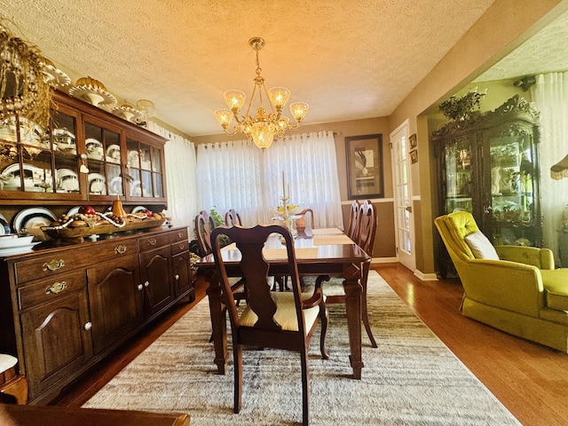 dining space with dark wood-style flooring, a textured ceiling, a notable chandelier, and baseboards