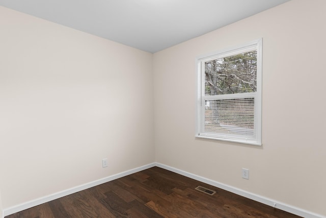 empty room with visible vents, dark wood-type flooring, and baseboards