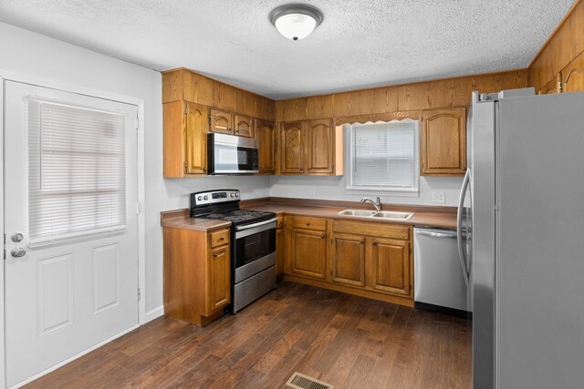 kitchen featuring visible vents, brown cabinets, a sink, dark wood-style floors, and appliances with stainless steel finishes