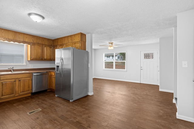 kitchen featuring visible vents, a sink, dark wood-style floors, stainless steel appliances, and brown cabinetry