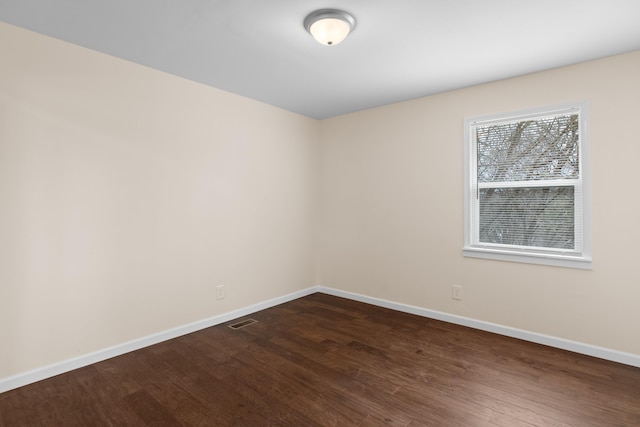 unfurnished room with visible vents, dark wood-type flooring, and baseboards