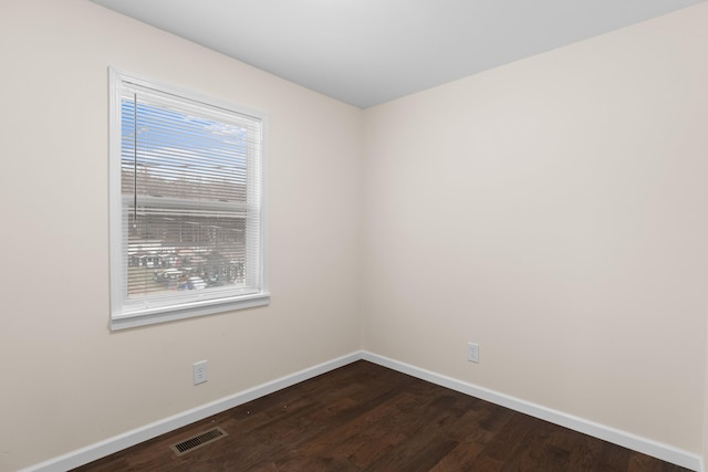 empty room with dark wood-style floors, visible vents, and baseboards