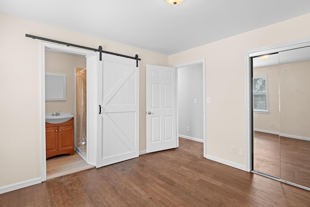 unfurnished bedroom featuring baseboards, a barn door, wood finished floors, a closet, and a sink