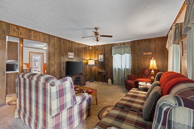 living room featuring ceiling fan, light colored carpet, plenty of natural light, and wood walls