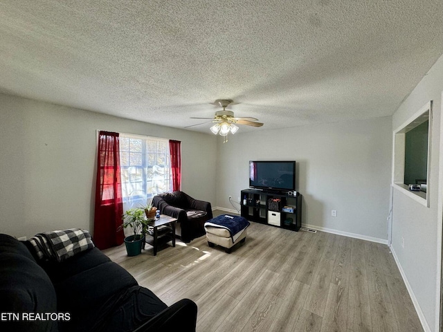 living room with a ceiling fan, light wood-style floors, baseboards, and a textured ceiling