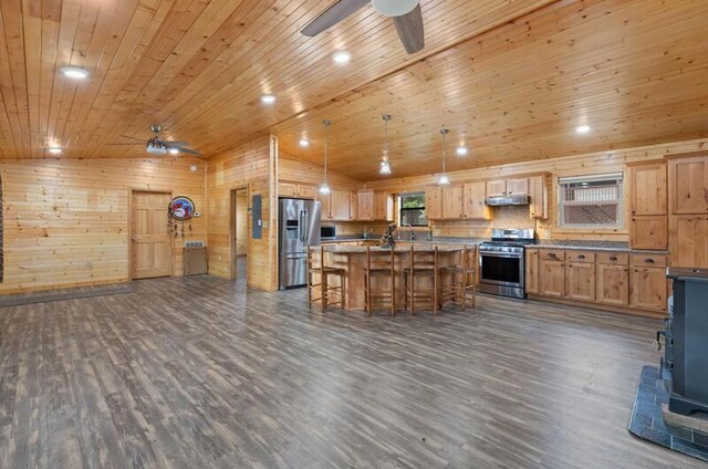 kitchen featuring a wood stove, hanging light fixtures, stainless steel appliances, lofted ceiling, and a breakfast bar