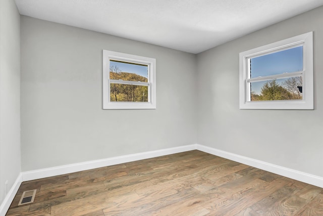 spare room featuring baseboards, wood finished floors, and visible vents