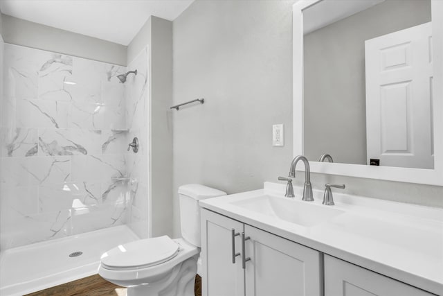 bathroom with toilet, vanity, wood finished floors, and a marble finish shower