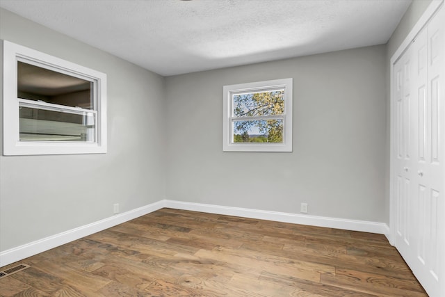 unfurnished bedroom featuring dark wood finished floors, visible vents, a closet, baseboards, and a textured ceiling