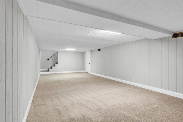 finished below grade area with a textured ceiling, stairs, wooden walls, carpet, and visible vents