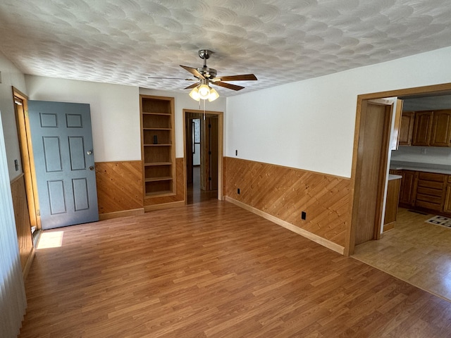 unfurnished room featuring a textured ceiling, hardwood / wood-style flooring, ceiling fan, and wood walls