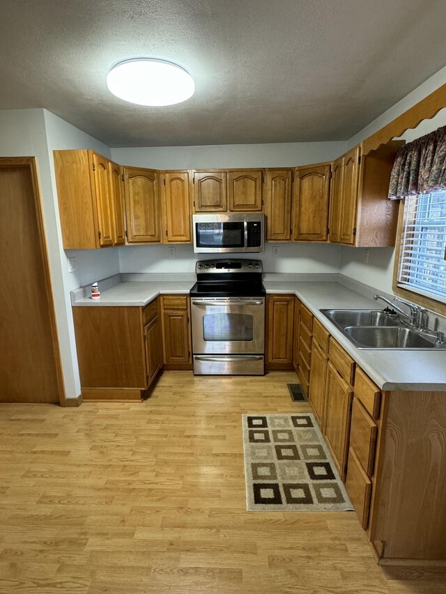 kitchen featuring appliances with stainless steel finishes, light wood-type flooring, a textured ceiling, and sink