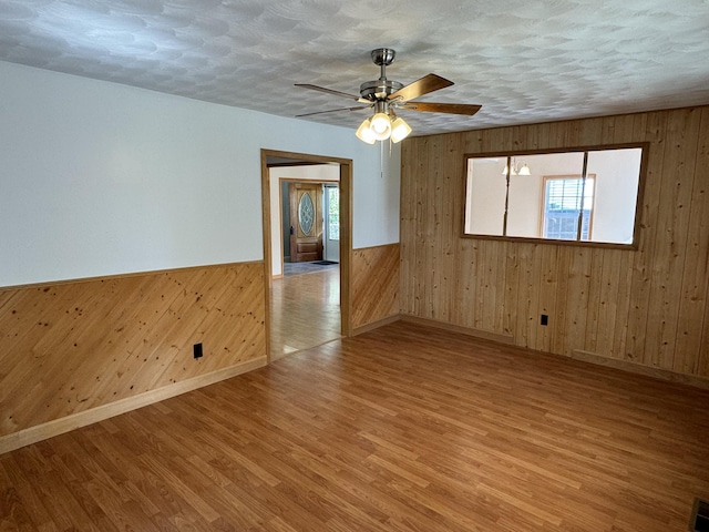 empty room with hardwood / wood-style floors, ceiling fan, wood walls, and a textured ceiling