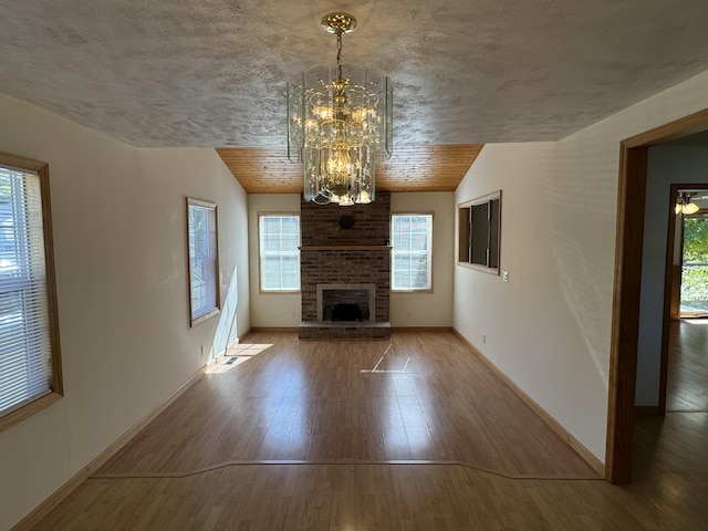 unfurnished living room featuring an inviting chandelier, hardwood / wood-style floors, vaulted ceiling, a fireplace, and wood ceiling