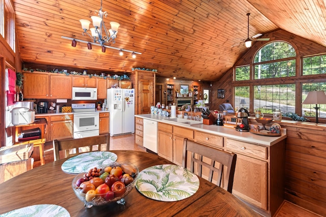 dining room with sink, rail lighting, high vaulted ceiling, wood walls, and ceiling fan with notable chandelier