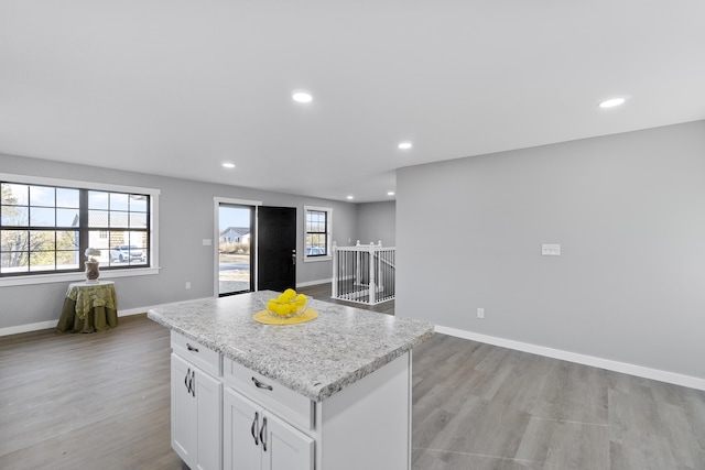 kitchen with light stone countertops, light wood-type flooring, a kitchen island, and white cabinets