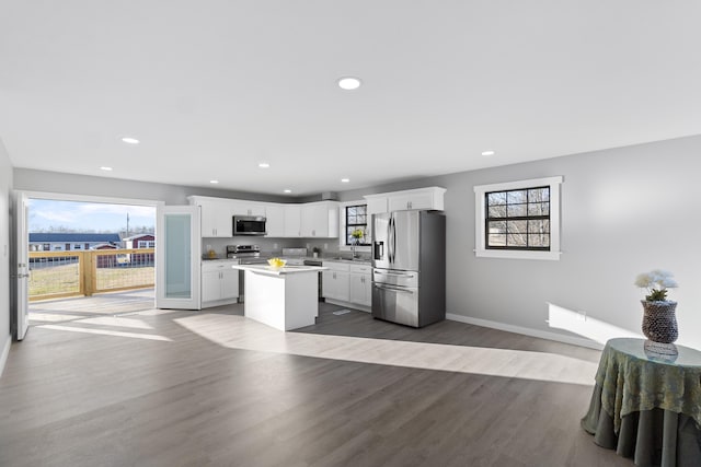 kitchen with appliances with stainless steel finishes, a kitchen island, hardwood / wood-style flooring, a healthy amount of sunlight, and white cabinets