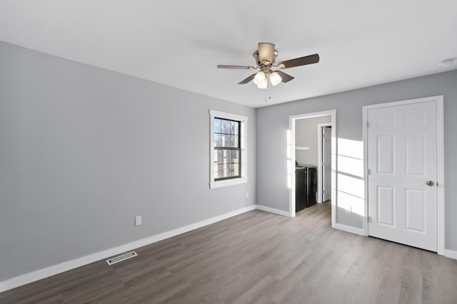 unfurnished bedroom featuring ceiling fan, a walk in closet, washing machine and clothes dryer, and light wood-type flooring