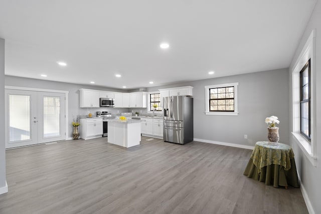 kitchen with a kitchen island, appliances with stainless steel finishes, light hardwood / wood-style flooring, white cabinets, and french doors