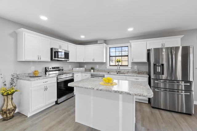 kitchen featuring sink, a center island, light wood-type flooring, stainless steel appliances, and white cabinets