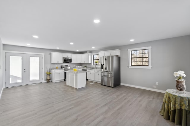 kitchen featuring appliances with stainless steel finishes, white cabinetry, light hardwood / wood-style flooring, a center island, and french doors