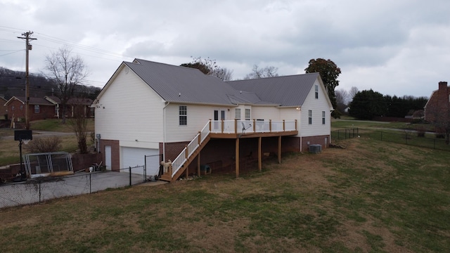 rear view of property featuring a lawn, a wooden deck, central AC unit, and a garage